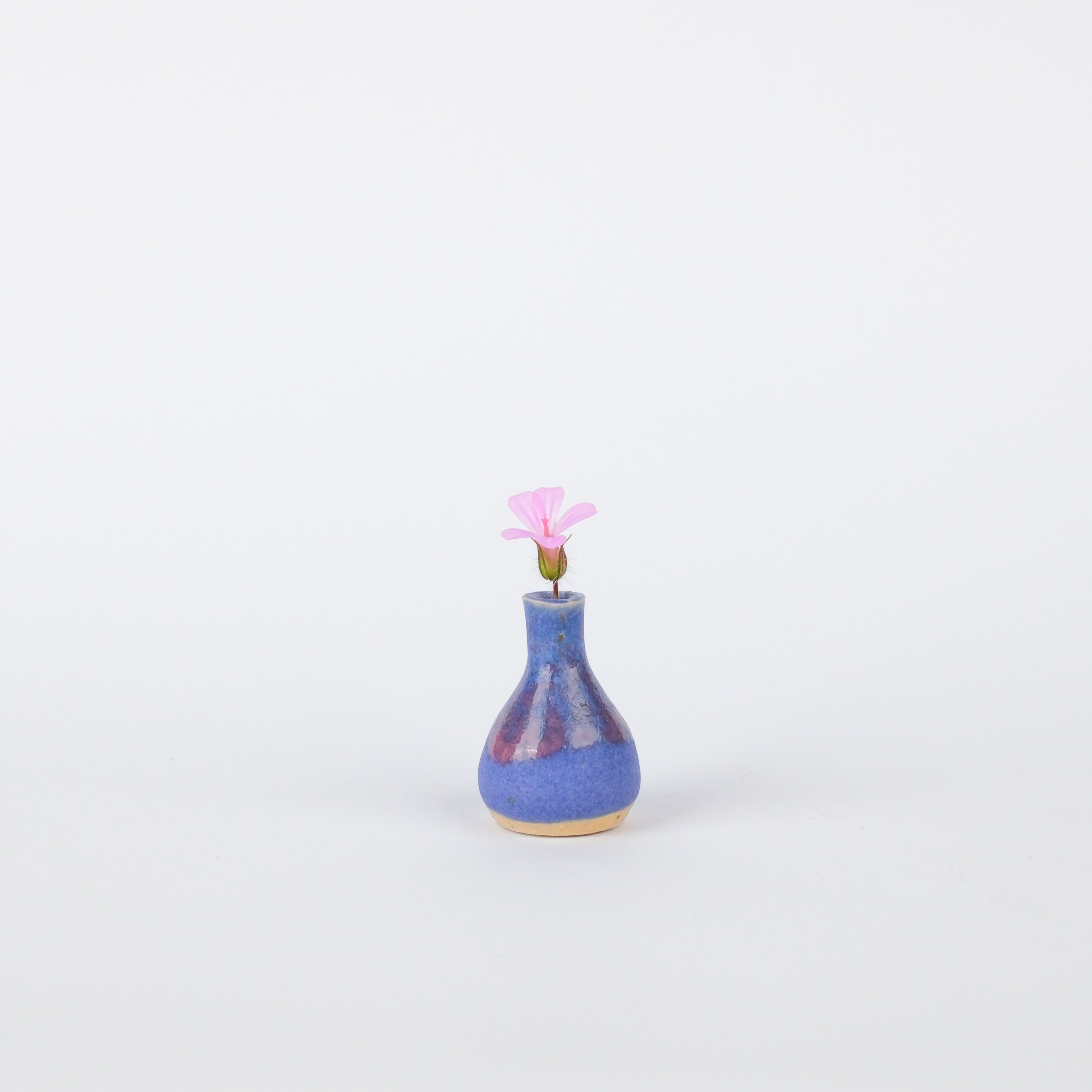 Handcrafted 29mm blue stoneware bud vase with a glossy finish and a single small pink flower on a white background.
