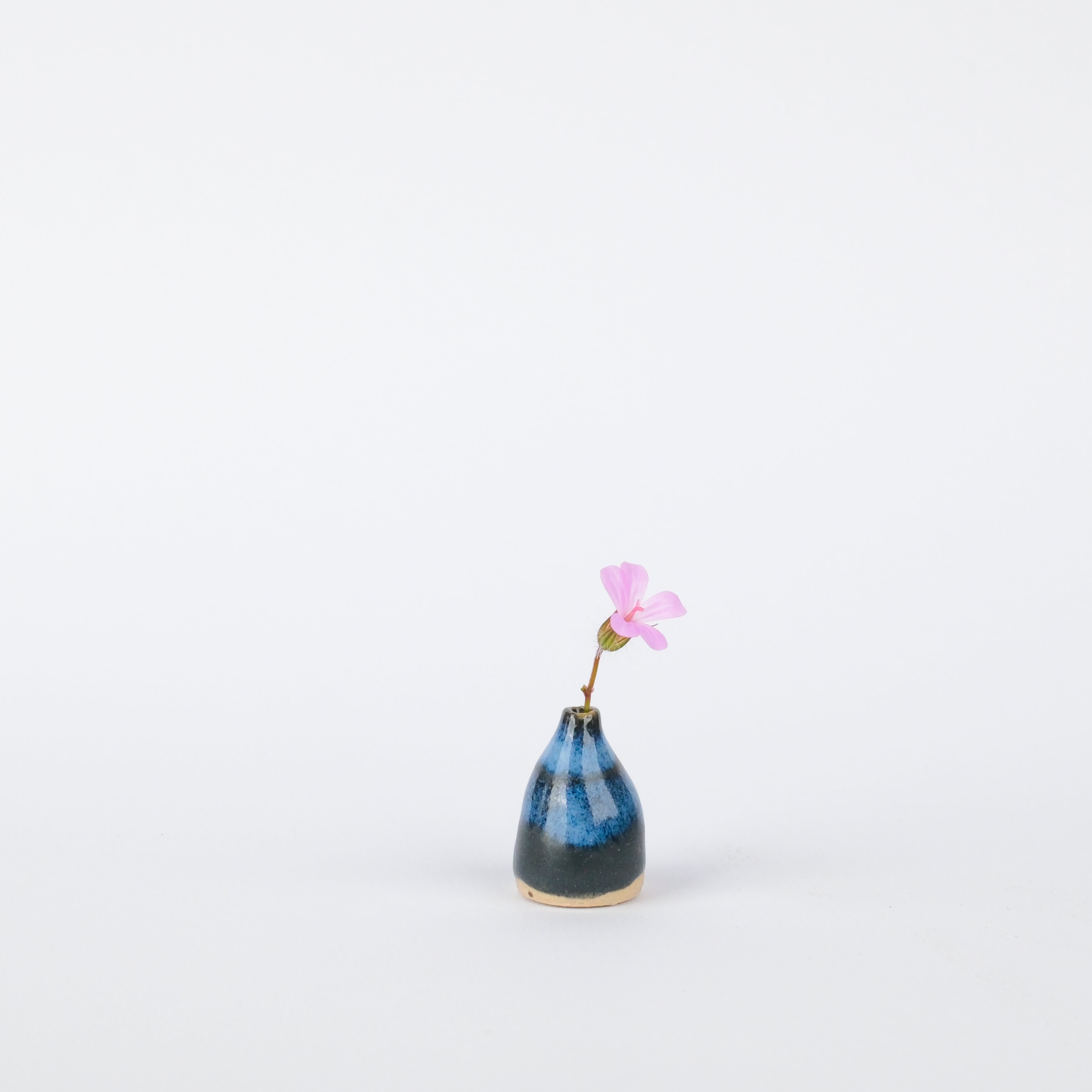 Handcrafted 25mm stoneware vase with a blue and black glazed finish holding a single small pink flower.