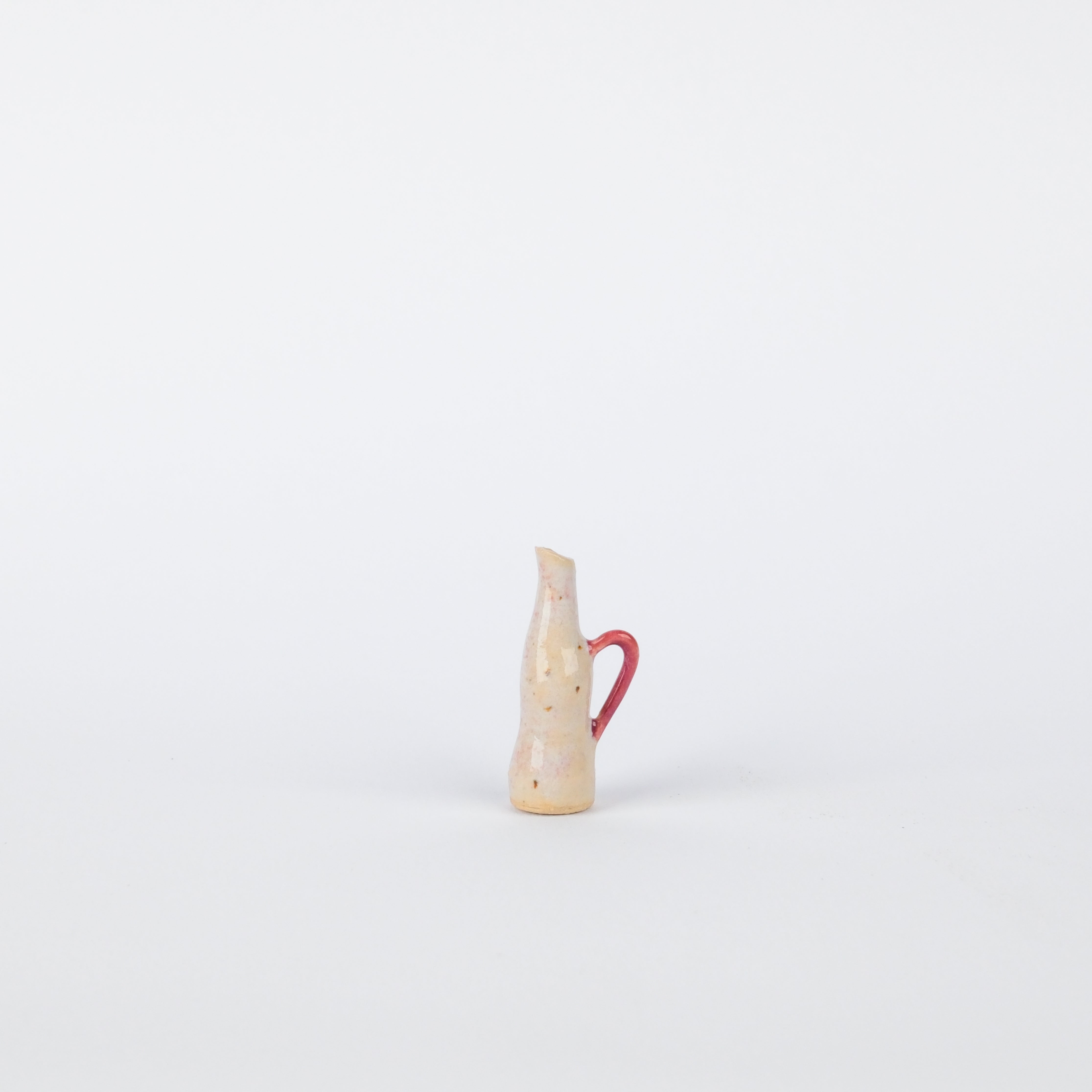 Small handmade speckled stoneware jug with a pink handle, 35mm tall, against a plain white background.