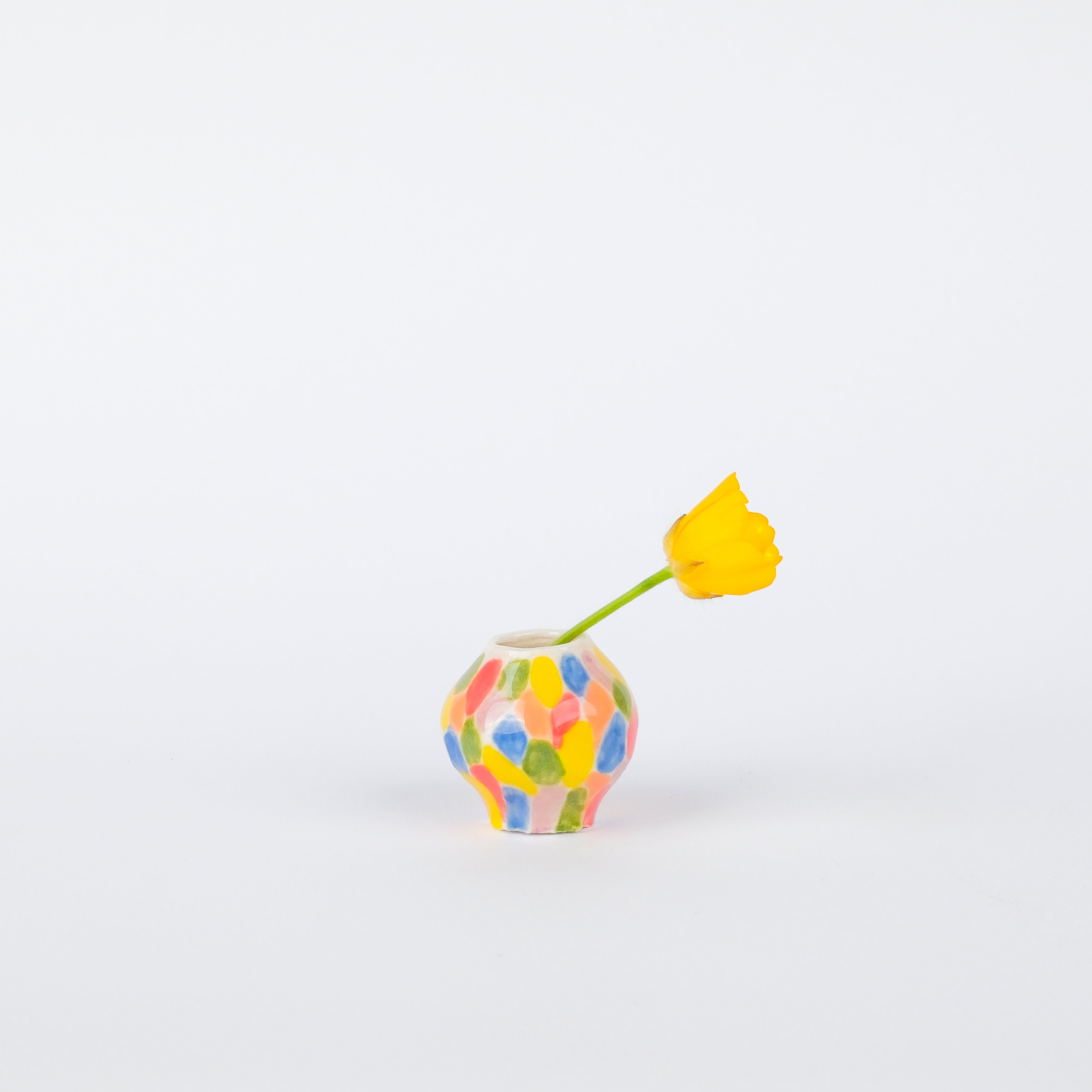 Hand-painted 25mm stoneware vase with a colorful speckled pattern, holding a single yellow flower.